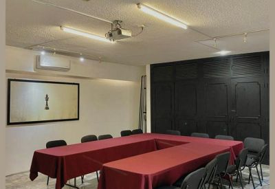 Meeting room with a U-shaped table covered in red cloth and black chairs.
