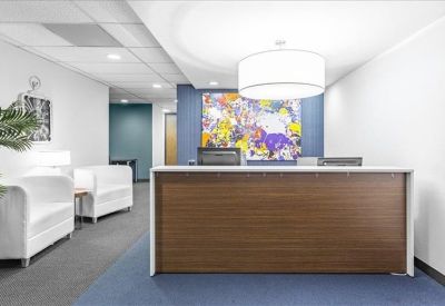 Reception area with a dark wood front desk, white seating, and vibrant abstract wall art.