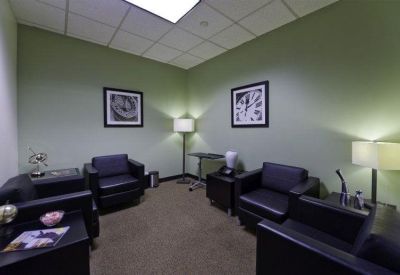 Breakout lounge with four black leather armchairs, green walls, and framed art.