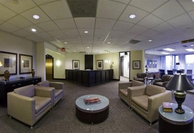Spacious reception lobby with beige armchairs, circular coffee table, and dark wood front desk.