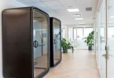 Two modern black privacy phone booths in a bright corridor with potted plants.