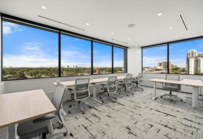 Bright coworking area with long white desks and large windows overlooking the city.