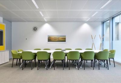 Spacious boardroom with a long white table, lime green chairs, and natural light from large windows.