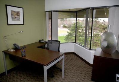 Private office with L-shaped desk, ergonomic chair, and large corner windows.