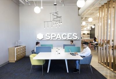 Coworking lounge with long white desks, colorful chairs, and a geometric chandelier.