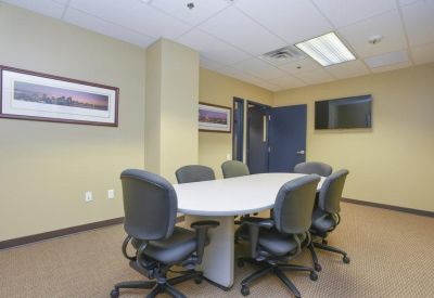 Small meeting room with an oval white table and grey upholstered chairs.