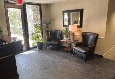 Reception area with tiled floor, dark wooden desk, and leather armchairs near a bright window.