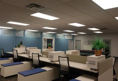 Well-lit open office floor with multiple rows of white workstations and blue benches.