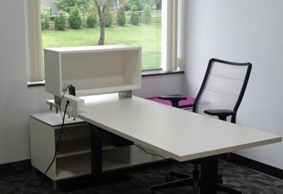 Private office with white sit-stand desk and large window showing greenery.