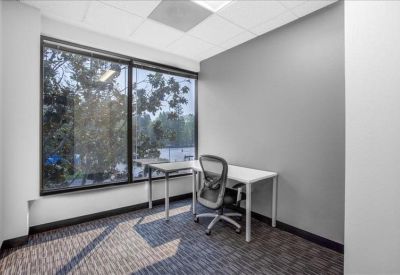 Corner office suite with an L-shaped desk and large window overlooking trees.
