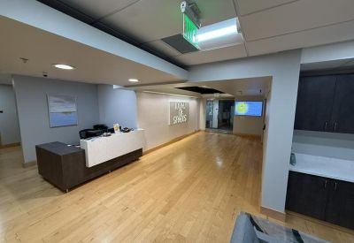 Modern reception lobby with white front desk, warm wood flooring, and recessed lighting.