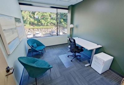 Private office featuring two teal velvet accent chairs and a white sit-stand desk by a window.