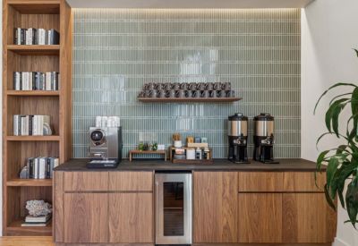 Sleek coffee station with wood cabinetry, a sage green tiled backsplash, and various beverage dispensers.