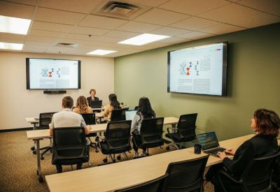Classroom-style training room with rows of desks, laptops, and large wall-mounted screens.
