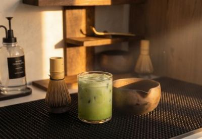 Close-up of a matcha latte on a dark mat alongside traditional bamboo tea whisks.