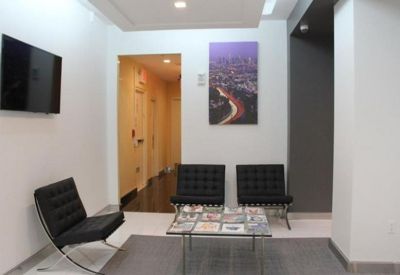 Small waiting area with black tufted chairs and a city skyline art piece.