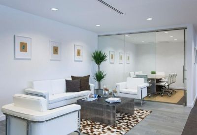 Modern lounge area with white leather sofas, abstract rug, and indoor plants.