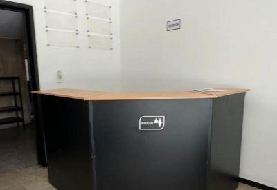 A black angular reception desk with a light wood countertop in a bright lobby.