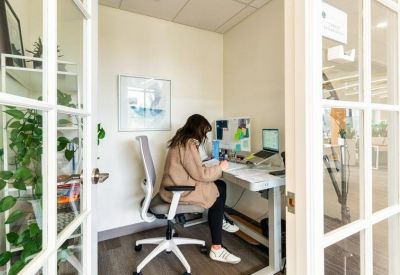 Private glass-walled office with a standing desk and ergonomic chair.