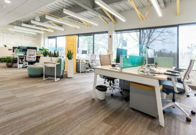 Bright open-plan coworking area with rows of desks and large windows.
