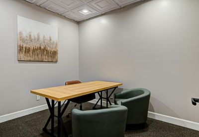 Small meeting room with a light wood table, grey armchairs, and abstract wall art.