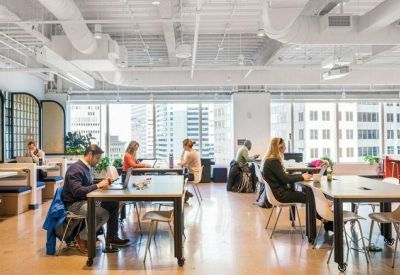 Bright open-plan coworking space with large shared tables and expansive city views.