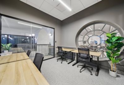 Shared office space with ergonomic chairs and a view through a large circular decorative window.