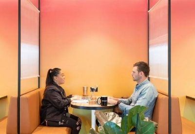 Two colleagues conversing in a private booth with warm orange walls and soft lighting.