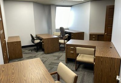Spacious shared office area with multiple wooden desks and ergonomic chairs.