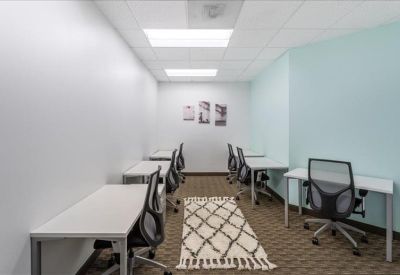 Brightly lit team room featuring several white desks and a patterned area rug.