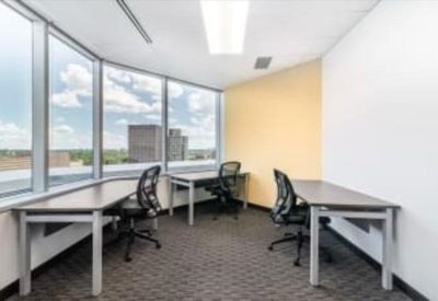 Bright corner office with multiple desks, black ergonomic chairs, and expansive city views.
