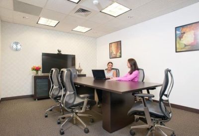 Professional meeting room with a dark wood conference table, mesh-back chairs, and video conferencing screen.