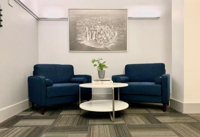 Communal lounge area with two blue armchairs, a round coffee table, and a large piece of wall art.