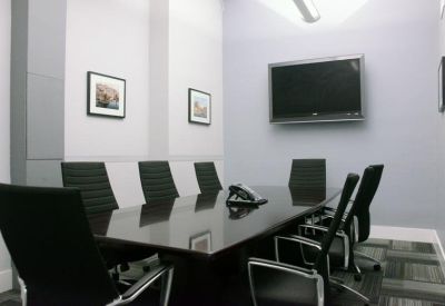 Sleek meeting room featuring a long dark wood table, black leather chairs, and a wall-mounted screen.