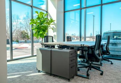 Bright workspace with white desks, ergonomic black chairs, and large windows overlooking the street.