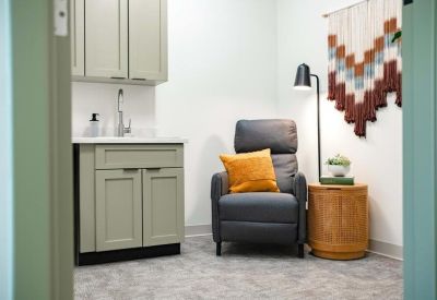 A quiet room featuring a grey recliner, a wooden side table, and a textile wall hanging.