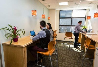 Coworking space with high-top wooden desks, orange stools, and hanging pendant lights.