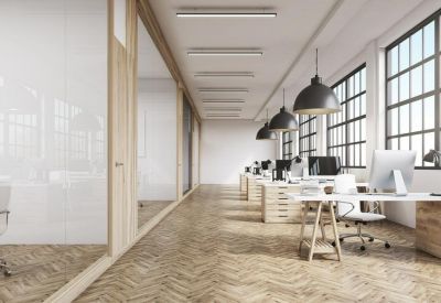 Bright, airy open-plan office with herringbone wood floors, large industrial windows, and rows of desks.
