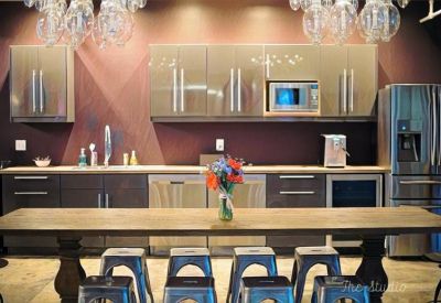 Communal kitchen area with sleek cabinetry, long wooden dining table, and industrial metal stools.