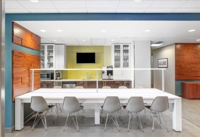 Modern communal kitchen and dining area featuring a long white table and grey chairs.