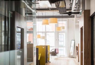 Bright glass-walled private office suites with white desks and black ergonomic chairs.