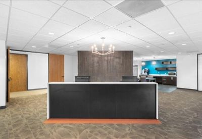 Modern reception area with a dark front desk, decorative chandelier, and kitchen in the background.