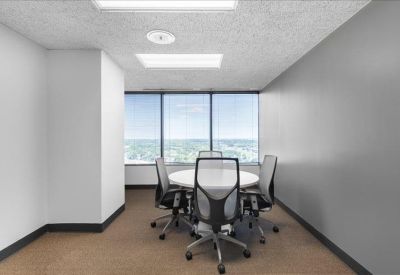 Bright conference room featuring a round white table, mesh chairs, and large windows.