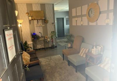 Comfortable waiting area with blue and grey armchairs, a large wall clock, and warm lighting.