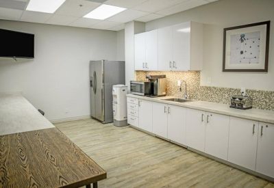 Communal kitchen and breakroom with white cabinetry and a long wooden dining table.