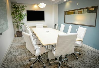Meeting room with white chairs, a large table, and a wall-mounted screen.