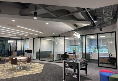 Modern communal area with a foosball table, colorful seating, and glass-walled offices.