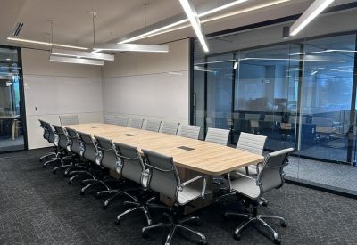 Spacious boardroom with a long light-wood table and grey ergonomic chairs.