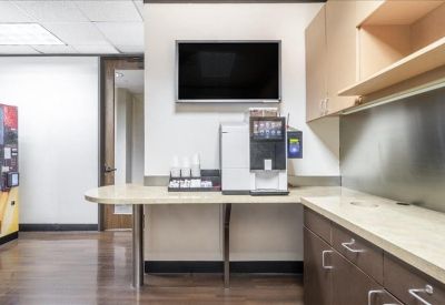 Modern breakroom area with a coffee machine, wall-mounted TV, and sleek cabinetry.