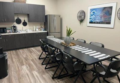 Modern communal kitchen and dining area at 3730, West Swift Avenue with a long table and dark cabinetry.